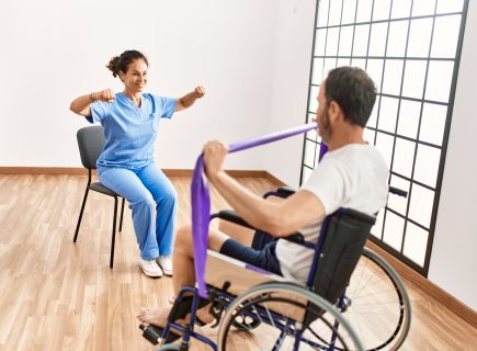 Persian Horizon middle age man woman having rehab session using elastic band sitting wheelchair physiotherapy clinic 1