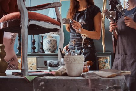 female-artist-with-her-assistant-aprons-painting-vintage-chair-with-paintbrush-workshop-scaled.jpg